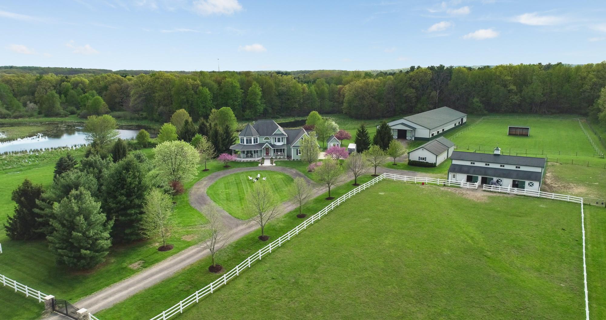 Aerial view of a horse farm with a house, barns and white-fenced pastures in Fenton