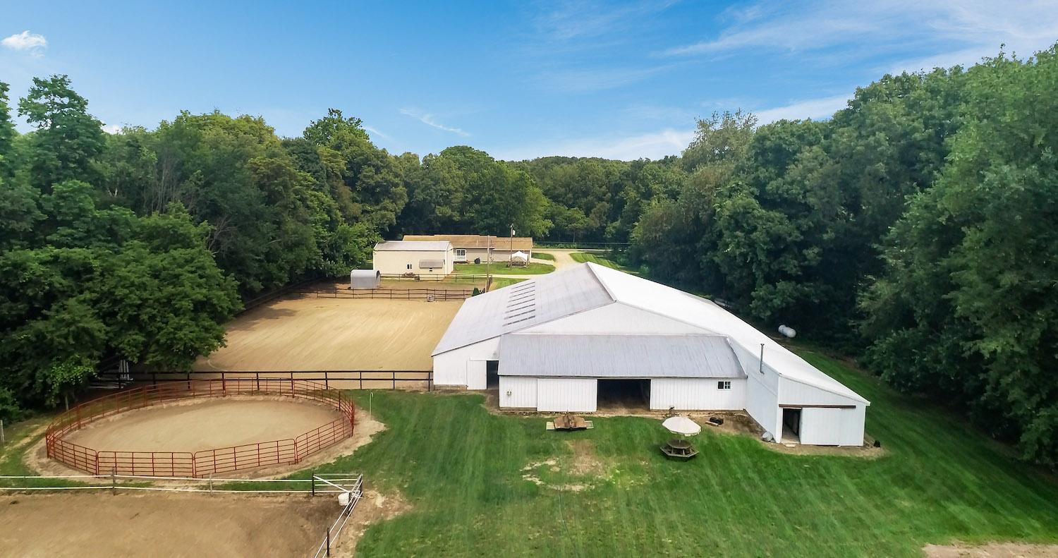 White barn and outdoor riding arena surrounded by trees in Kalamazoo County