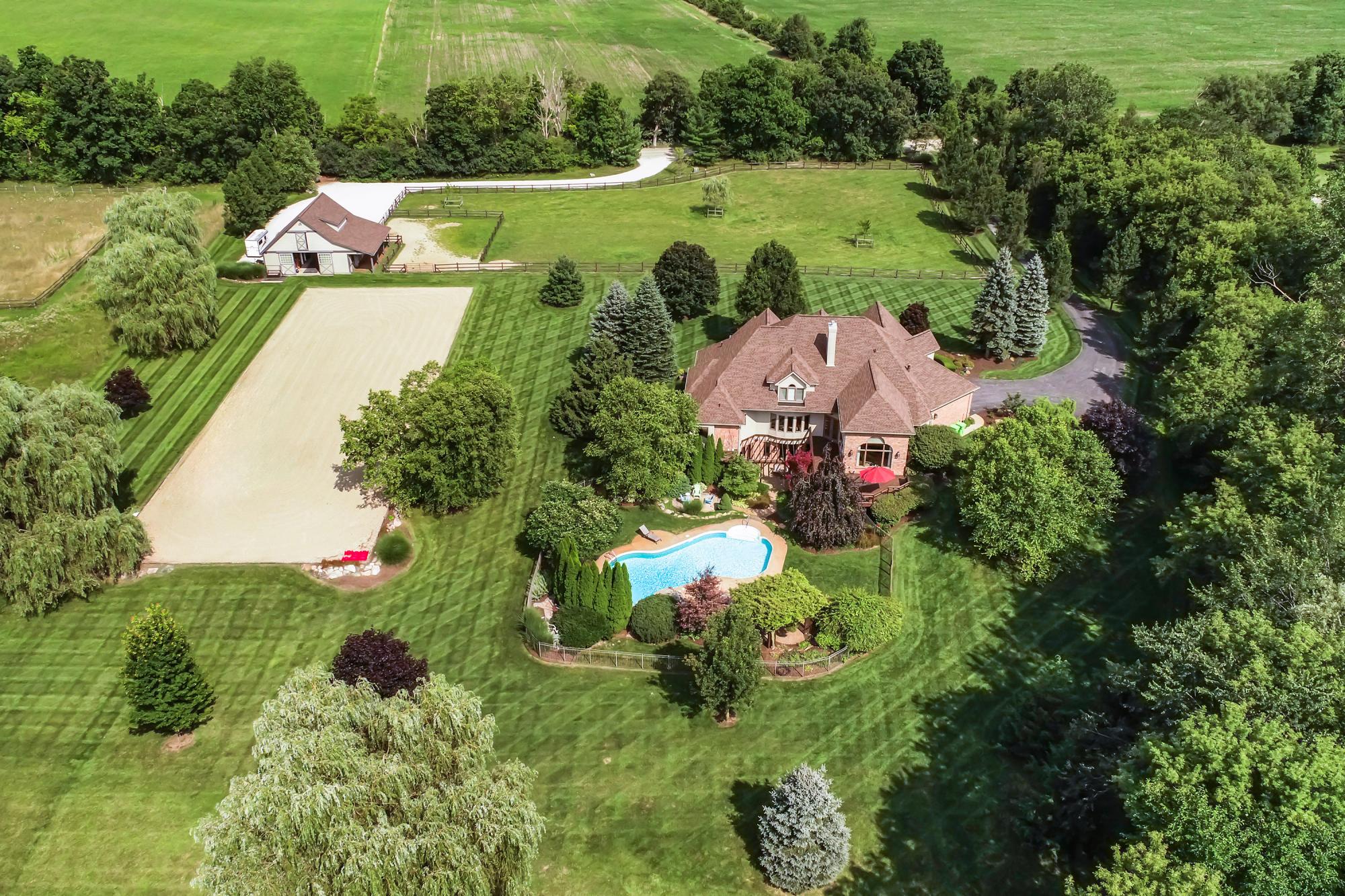 Aerial view of a brick home with an inground pool and fenced pastures in Dexter